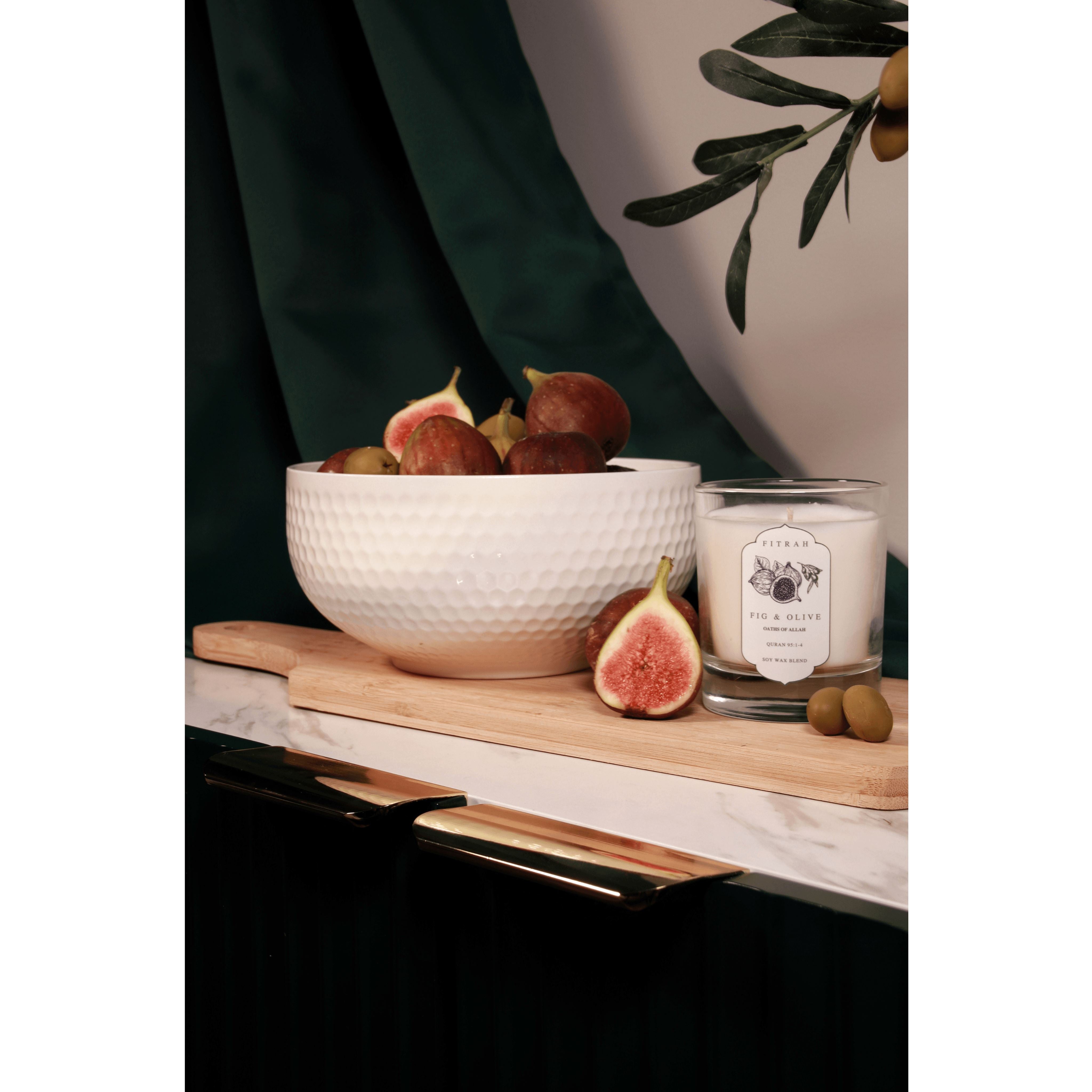 a bowl of figs with a couple olives along with the figs and olive candle from the oaths of allah collection